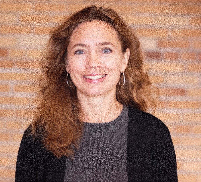 Kristin Persson Posing ofr a photo infront of a red and brown brick wall